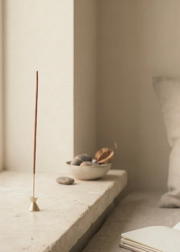 Incense stick on a stone surface with a bowl of stones and a book in the background.